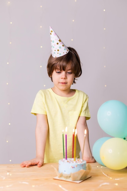 Ragazzino sveglio di compleanno in torta di cappello con palloncini di candele buon compleanno
