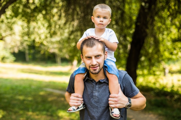 Ragazzino sveglio e il suo bel giovane papà seduto sulle spalle di suo padre mentre riposa nel parco