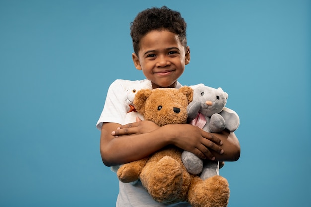 Ragazzino sveglio felice con due peluche e orsacchiotto che ti sorride mentre giochi