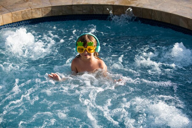 Ragazzino sveglio in occhiali da sole divertenti in piscina in una giornata di sole