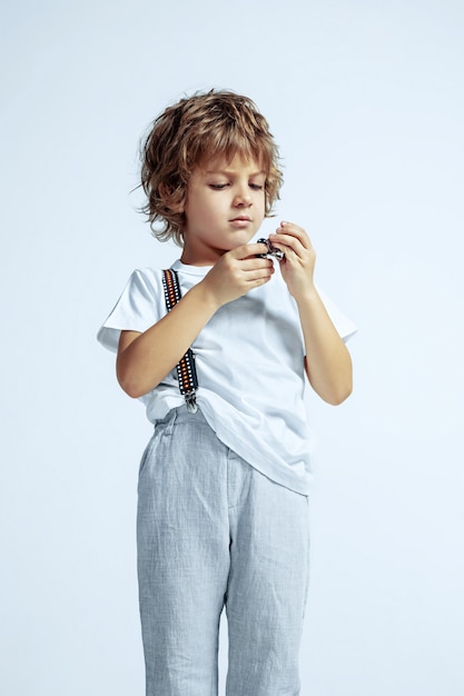 Ragazzo abbastanza giovane in abiti casual sul muro bianco. Posa alla moda, sembra sicuro. Bambino in età prescolare maschio caucasico con emozioni facciali luminose. Infanzia, espressione, divertimento.