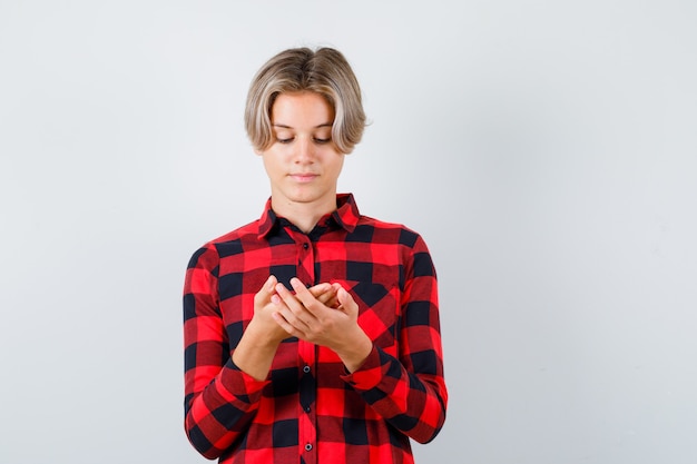 Ragazzo abbastanza teenager che guarda il suo palmo in camicia a quadri e sembra concentrato, vista frontale.