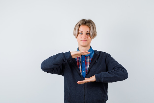 Ragazzo adolescente carino in camicia, felpa con cappuccio che mostra il segno della taglia e sembra allegro, vista frontale.