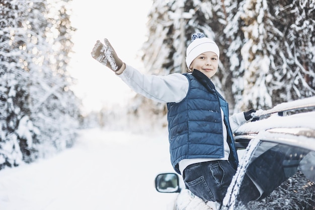 Ragazzo adolescente che guarda fuori dal finestrino dell'auto che viaggia nella foresta innevata d'inverno Avventura di viaggio su strada e concetto di viaggio locale Bambino felice che si gode il giro in macchina Vacanze invernali di Natale e vacanze di Capodanno