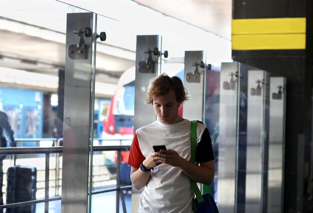 Ragazzo adolescente che usa lo smartphone alla stazione ferroviaria