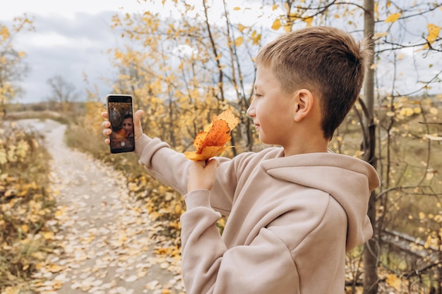 Ragazzo adolescente con bouquet autunnale di foglie d'acero che scatta foto selfie con il suo smartphone