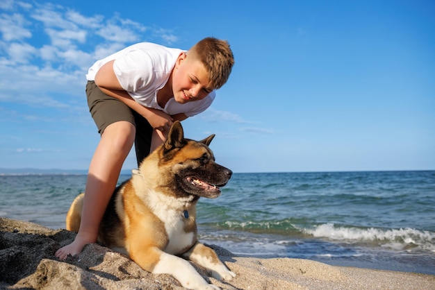 Ragazzo adolescente con capelli biondi e guinzaglio in mano gioca e cammina con il cane di razza Akina Inu sulla spiaggia selvaggia lungo il Mar Nero