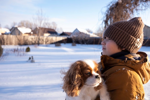 Ragazzo adolescente con un animale domestico che si diverte con la neve Cuccino carino in inverno Cavalier King Charles Spaniel