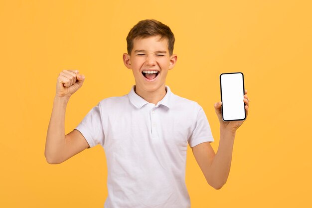 Ragazzo adolescente eccitato che tiene in mano uno smartphone con lo schermo vuoto e celebra il successo
