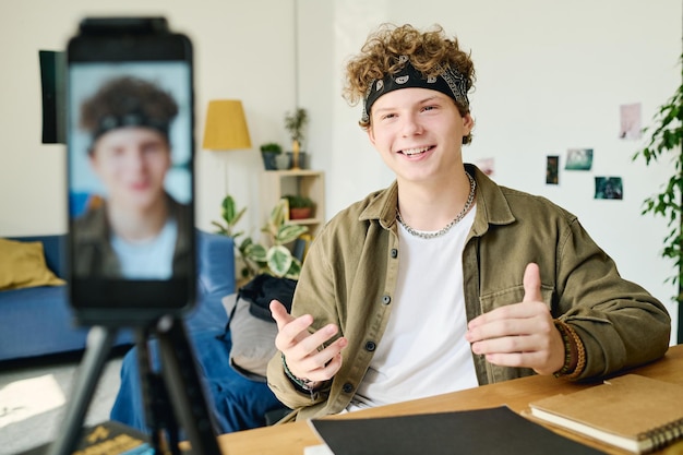 Ragazzo adolescente felice in abbigliamento casual che parla al pubblico online durante il livestream