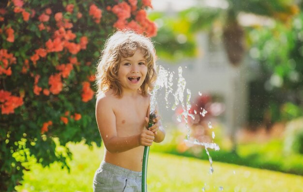 Ragazzo adorabile che innaffia le piante dallo spruzzo del tubo flessibile con il tubo dell'acqua nel giardino sul cortile