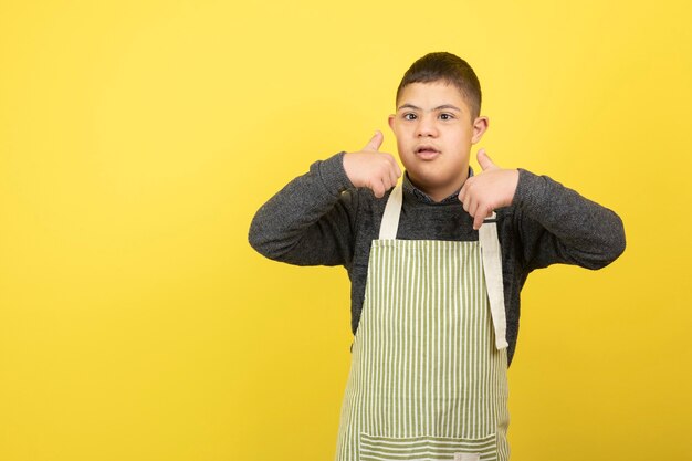 Ragazzo adorabile con sindrome di down in grembiule che dà i pollici in su.