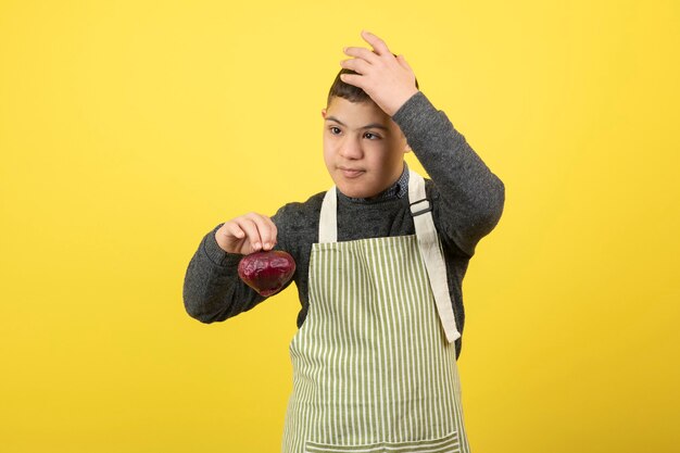 Ragazzo adorabile con sindrome di down in grembiule che tiene cipolla rossa.