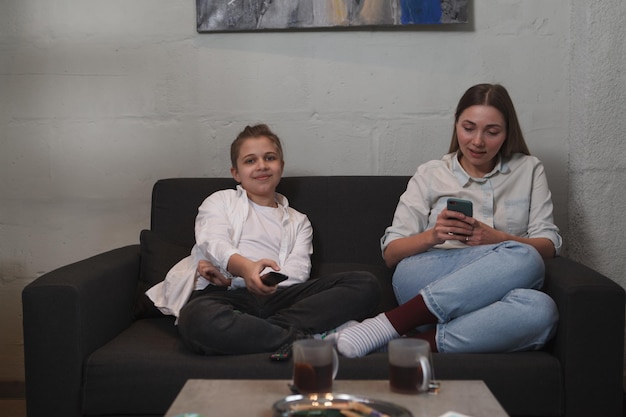 Ragazzo affascinante che guarda la tv mentre sua madre usa lo smartphone