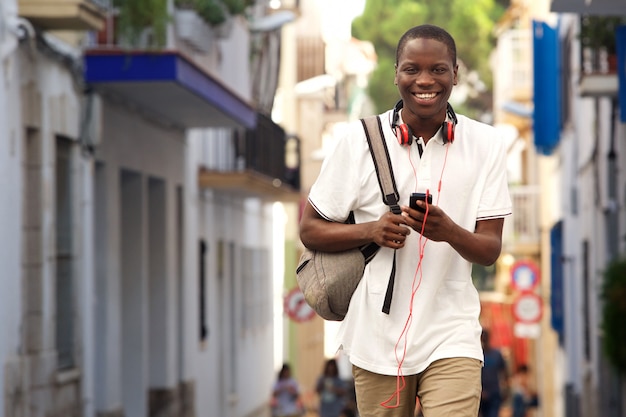 Ragazzo africano che cammina sulla strada con un telefono