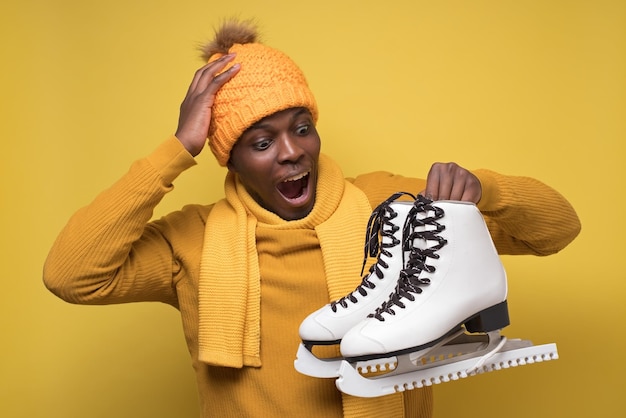 Ragazzo africano confuso con cappello e maglione e sciarpa tiene i pattini nelle sue mani