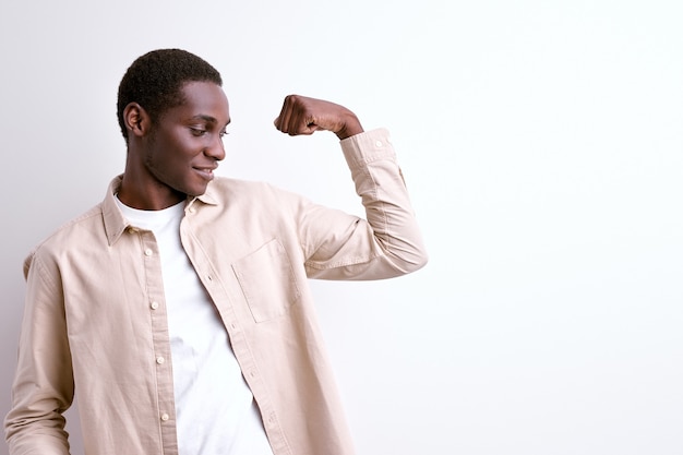 Ragazzo afroamericano che mostra i muscoli del braccio, potente uomo forte isolato su sfondo bianco studio