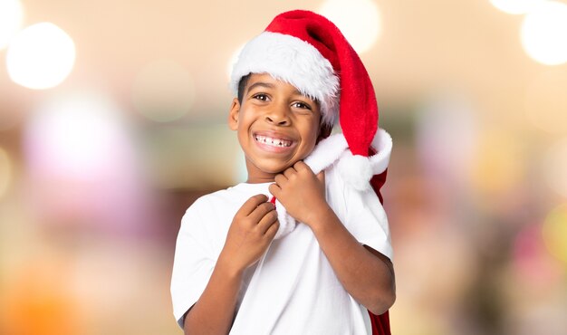 Ragazzo afroamericano con il cappello di natale e prendere una borsa con i regali sopra fondo vago