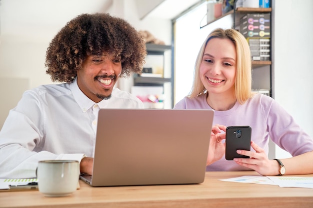 Ragazzo afroamericano e ragazza caucasica in una seduta di coworking che lavora su un computer portatile sorridente