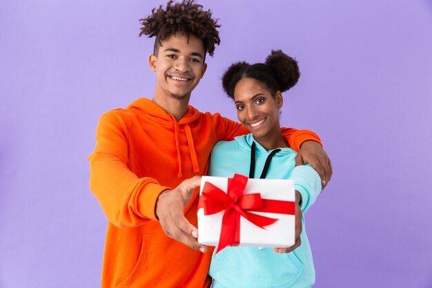 ragazzo afroamericano e ragazza sorridente mentre si tiene insieme confezione regalo, isolato sopra il muro viola
