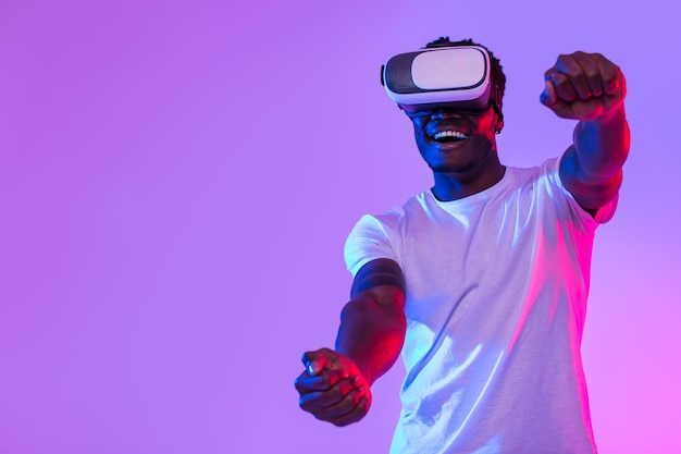 Ragazzo afroamericano eccitato in cuffia vr che gioca online in realtà virtuale che guida l'immaginario