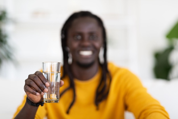 Ragazzo afroamericano sorridente liquido sano che tiene in mano un bicchiere d'acqua