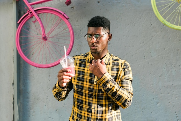 Ragazzo afroamericano spensierato in abbigliamento casual che tiene fresco sfondo estivo urbano cocktail tropicale