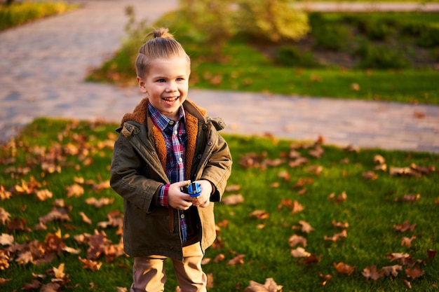 Ragazzo alla moda che si diverte nel parco cittadino autunnale e tiene in mano un giocattolo bambino felice che cammina tra
