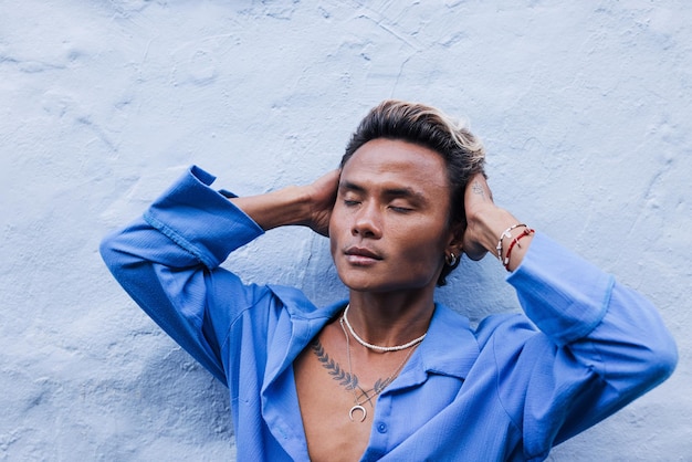 Ragazzo alla moda con una camicia blu appoggiata a un muro che si tocca la testa con gli occhi chiusi