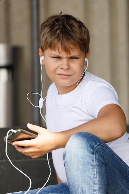 Ragazzo alla moda in cuffia con smartphone che ascolta musica nel parco