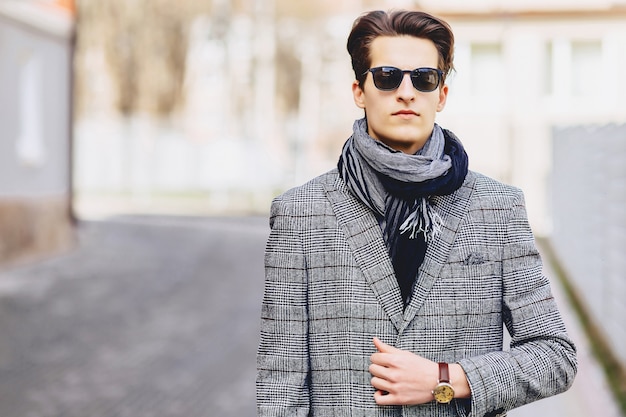 Ragazzo alla moda in occhiali da sole in cappotto con la cartella sulla strada