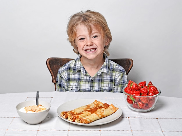 Ragazzo alla tavola di prima colazione che mangia i pancake e le fragole