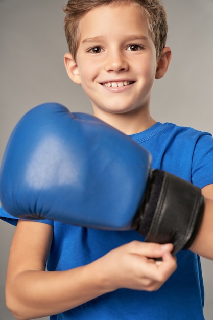 Ragazzo allegro che indossa i guantoni da boxe su sfondo grigio