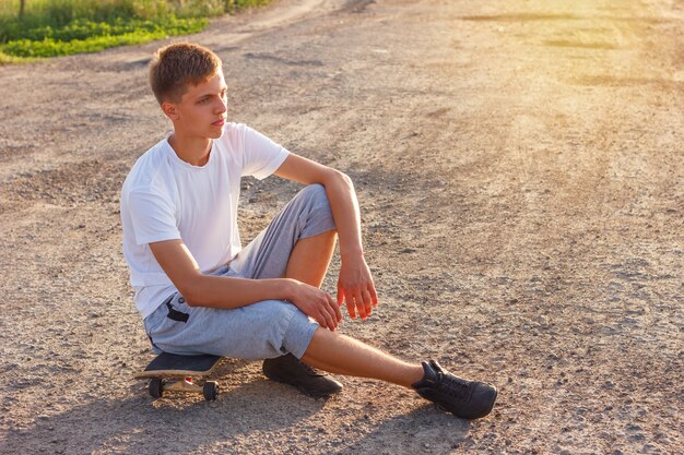 Ragazzo allegro che si siede su uno skateboard sulla strada in una giornata di sole