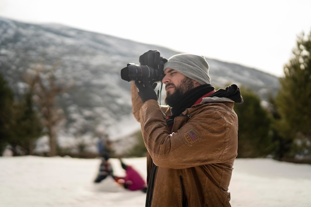ragazzo alto con barba e macchina fotografica che scatta foto nella neve