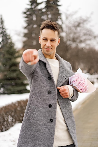 Ragazzo amico con un mazzo di fiori rosa ortensia in attesa della sua ragazza all'aperto mentre la neve sta cadendo. Concetto di San Valentino, proposta di matrimonio. l'uomo va ad un appuntamento.