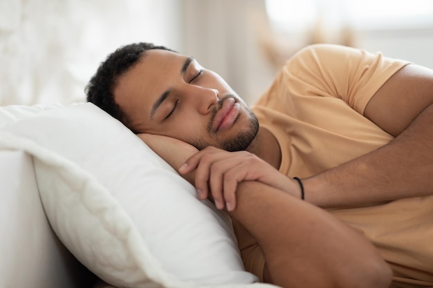 Ragazzo arabo che dorme sdraiato a letto facendo un pisolino nella camera da letto moderna