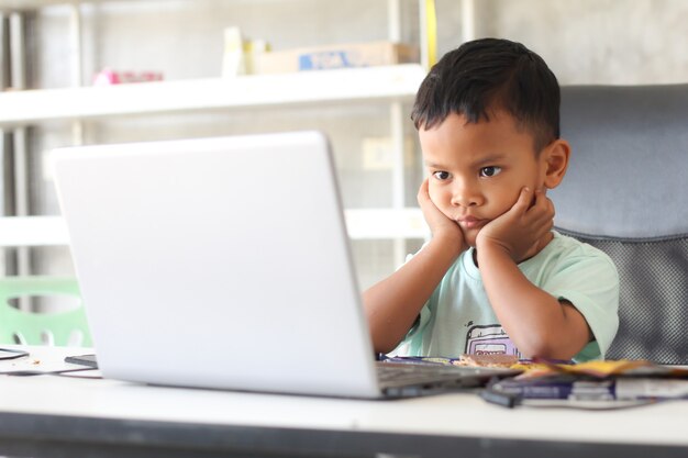 Ragazzo asiatico bambino seduto a tavola con il computer portatile e si prepara a scuola. Concetto di formazione online. Studio della lezione di lezione di videoconferenza online.