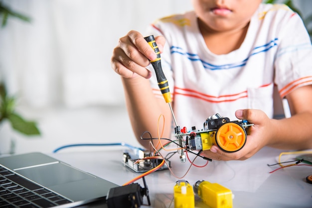 Ragazzo asiatico che assembla il progetto di compiti a casa dell'auto del robot Arduino a casa