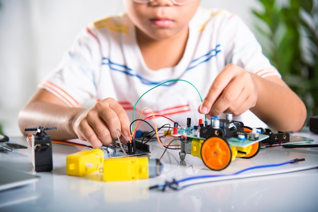 Ragazzo asiatico che collega l'energia e il cavo del segnale al chip del sensore con l'auto robot Arduino