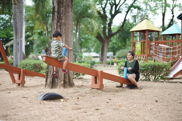 Ragazzo asiatico che gioca altalena e divertirsi con sua madre al parco giochi per bambini