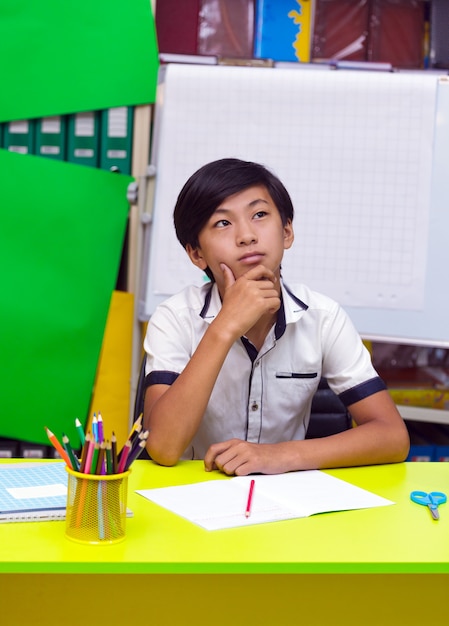 Ragazzo asiatico che pensa seduto in classe.