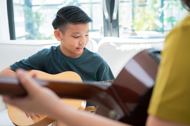 Ragazzo asiatico che suona la chitarra con il padre in soggiorno per insegnargli a suonare la chitarra al figlio