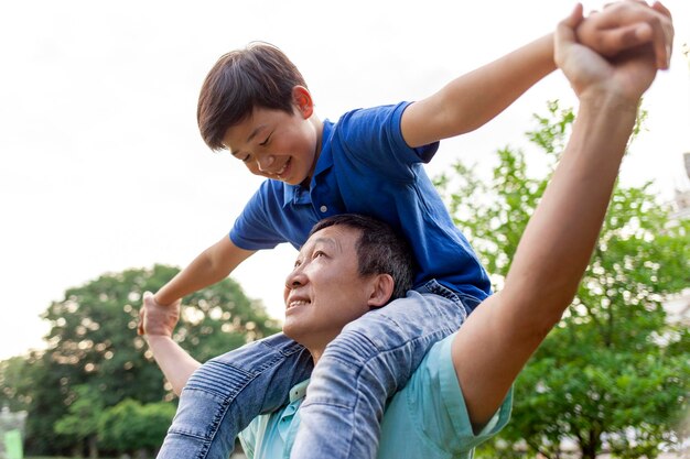 ragazzo asiatico che vola in avanti sulla schiena di papà pensionato coreano anziano che gioca con il figlio in estate