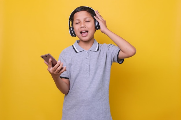 Ragazzo asiatico in stile casual che utilizza cuffie wireless e smartphone canta mentre si gode la musica a