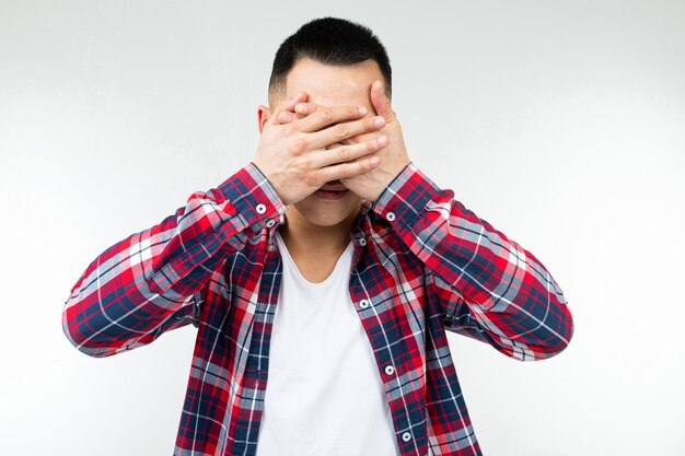 Ragazzo asiatico in una camicia a scacchi spalancata chiude gli occhi su uno sfondo bianco isolato per studio.