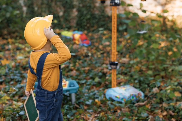 Ragazzo asiatico sveglio del costruttore del ragazzino che indossa il casco giallo protettivo sulle gru di costruzione del fondo