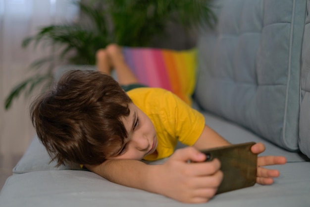 Ragazzo assonnato che gioca al telefono sdraiato sul divano dipendenza dai gadget superlavoro apatia