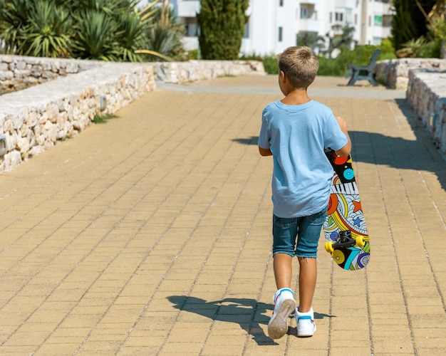 Ragazzo bambino che cammina con uno skateboard in mano nel parco