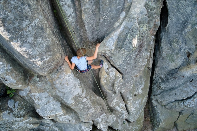 Ragazzo bambino che scala una parete ripida di una montagna rocciosa Lo scalatore per bambini supera un percorso impegnativo Impegnandosi nel concetto di sport estremo